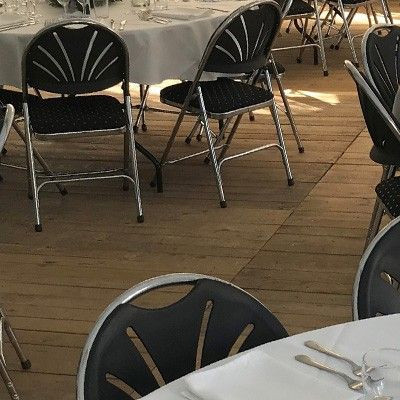 Des tables rondes dans une tente, couvertes de nappes blanches et entourées de chaises noires. Les tables sont prêtes pour un événement ou un repas.