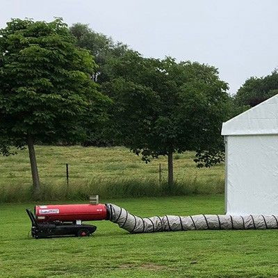 Un appareil de chauffage extérieur rouge relié à un long tuyau flexible, utilisé pour chauffer des espaces ouverts ou des tentes lors d'événements en plein air.