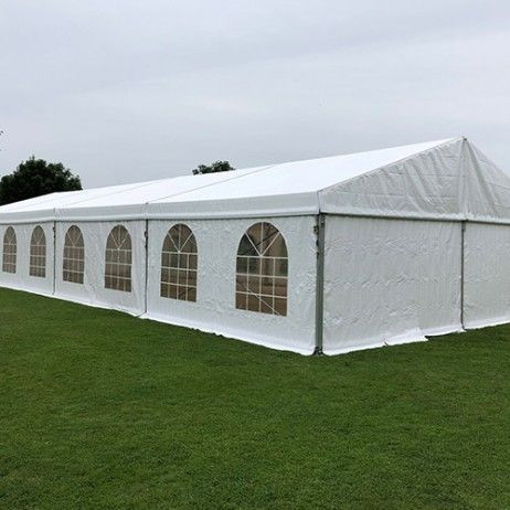 Un grand chapiteau blanc installé sur une pelouse verte. Le chapiteau est de grande taille et semble prêt pour un événement en plein air. Il y a des fenêtres en forme d'arcs sur le côté, laissant entrer la lumière naturelle.