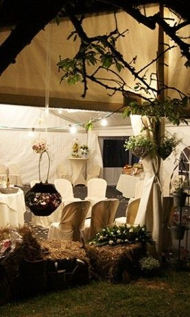 L'intérieur d'une tente décorée pour un événement festif. Les tables sont couvertes de nappes blanches et sont entourées de chaises avec des housses blanches. Les tables sont décorées avec des arrangements floraux et des bougies, créant une ambiance roman