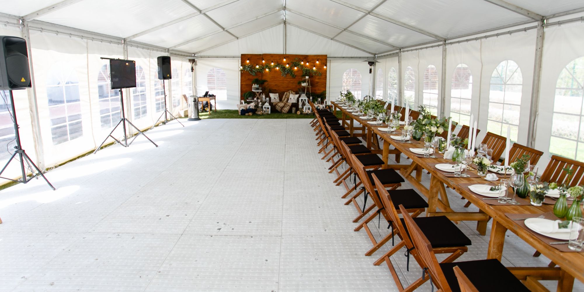 Une longue table de banquet dans une tente blanche, décorée avec des nappes blanches et des chaises en bois. Des arrangements floraux et des bouteilles d'eau sont placés sur la table, prête pour un dîner.